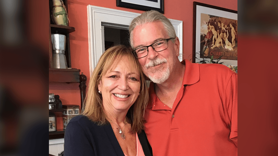 A smiling woman and man pose together in a cozy indoor setting.