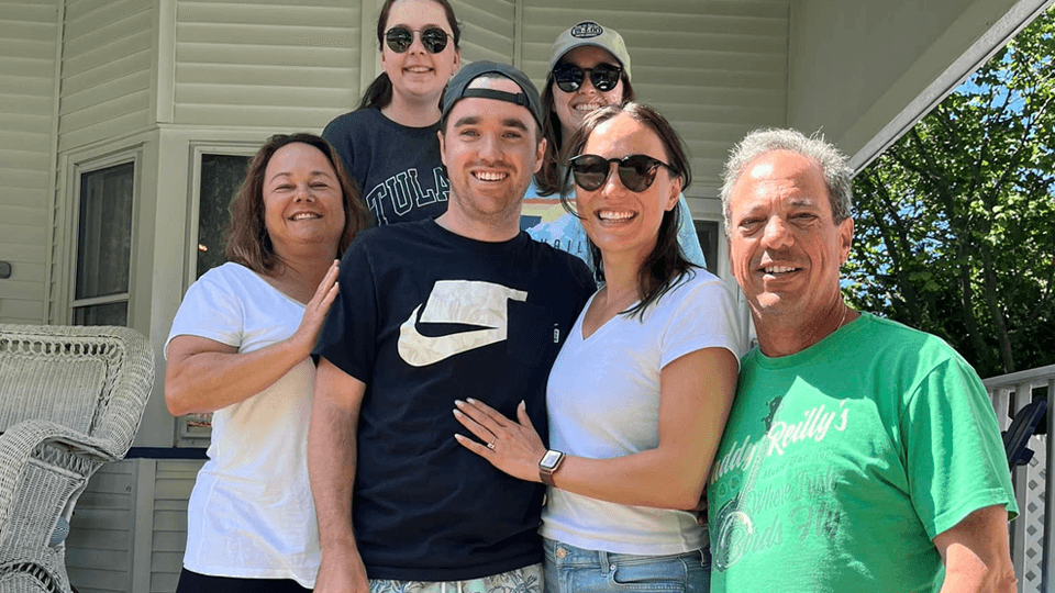 A group of six people smiling together on a porch.